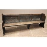 A stained pine pew, late 19th/early 20th century, the canted and shaped end supports united by a