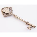 A silver coloured presentation key, the key with two cartouches within an openwork scroll border,