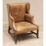 A George III style mahogany and tan leather wing back armchair, 19th century, the shaped wing