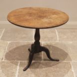 A George III oak tripod table, the circular plank top upon a baluster pedestal and three cabriole