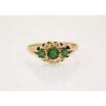 An emerald and diamond 9ct gold ring, the three graduated round cut emeralds within a border of