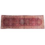 A large terracotta ground Persian runner, in red, blue and ivory colourways, the seven lozenge