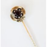 A garnet set yellow metal stick pin, the round cut garnet cut down set within a flower head designed