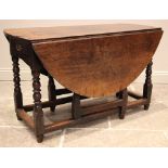 An 18th century oak drop leaf table, the oval plank top over a single frieze drawer, upon bobbin and