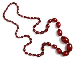 A string of cherry coloured 'amber' beads, the graduated oval beads strung upon string, largest bead