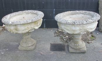 A pair of reconstituted stone garden urns, of compressed campana form, moulded with swag detail to