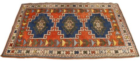 A Caucasian wool rug, with three central blue geometric medallions upon a terracotta ground,