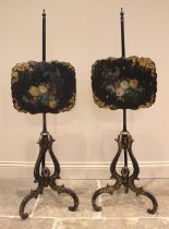 A pair of Victorian papier mache ebonised pole screens, each with a scalloped panel painted with a