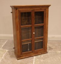 A Victorian and later, pine wall mounted display cabinet, the two glazed cupboard doors opening to