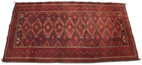 A Caucasian hand knotted wool rug, the central red field with ten linked serrated lozenges, enclosed