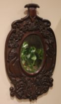 A carved oak wall mirror, late 19th century, the central oval mirror plate within a frame carved