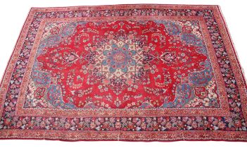 A Mashad wool carpet, the central blue medallion upon a vibrant red ground with foliate detail,