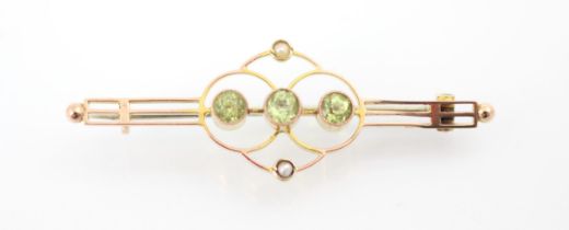 An Edwardian style peridot bar brooch, the three round cut peridots within sinuous mount with split