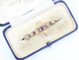 An Edwardian style garnet bar brooch, the oval cut garnet within openwork mount with split pearl
