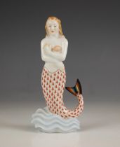 A Herend porcelain mermaid, 20th century, decorated with red fishnet tail, stood upon on a