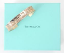 A Tiffany and Co silver cuff style bangle, the concave exterior with engraved writing throughout,