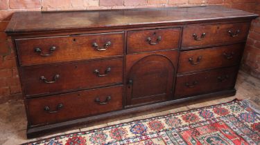 An early George III oak dresser base, the cleated plank top over a central arched cupboard door,