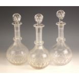 Three clear glass decanters and associated stoppers, each of globe and shaft form, with faceted ring