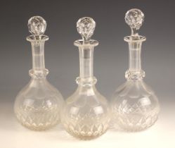 Three clear glass decanters and associated stoppers, each of globe and shaft form, with faceted ring