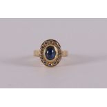An 18 kt 750/1000 gold entourage ring with a cabochon cut blue sapphire around it, 12 brilliants