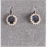 A pair of 14 kt 585/1000 white gold earrings, set with oval faceted sapphire and an entourage of