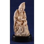 A carved ivory sculpture of a man with a bowl in his hand and a rabbit at his side, on wooden