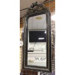 A rectangular mirror in a black ornamental frame and floral crown with, among other things, a