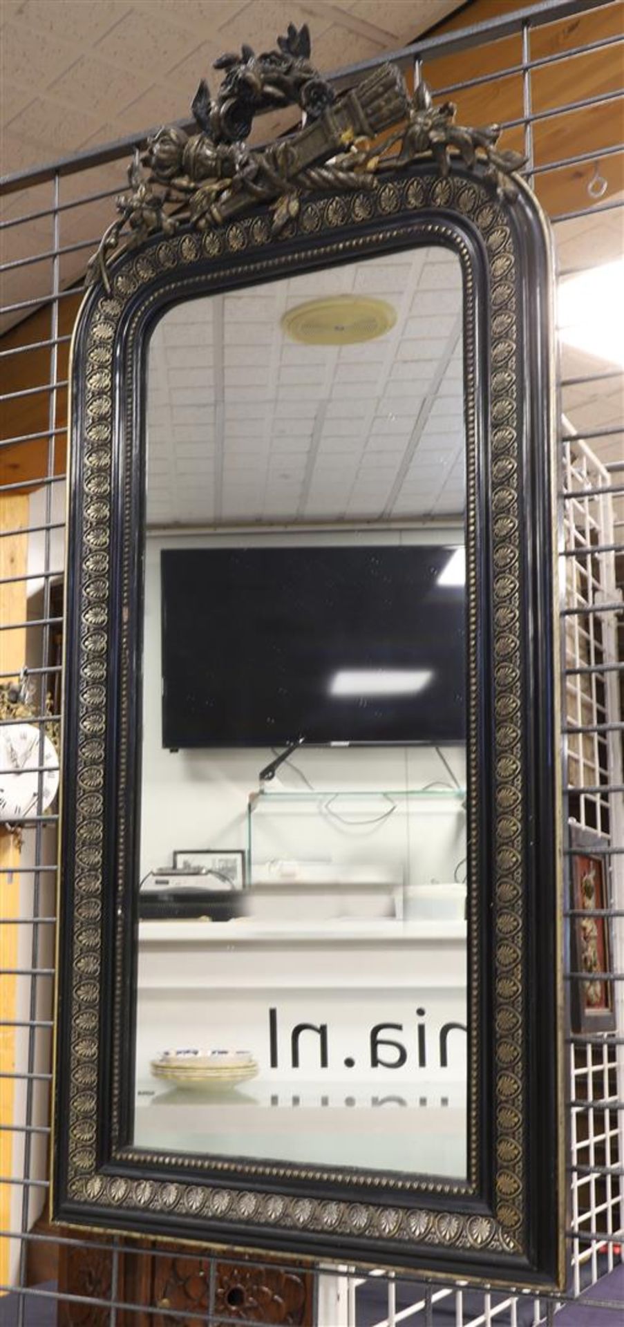 A rectangular mirror in a black ornamental frame and floral crown with, among other things, a