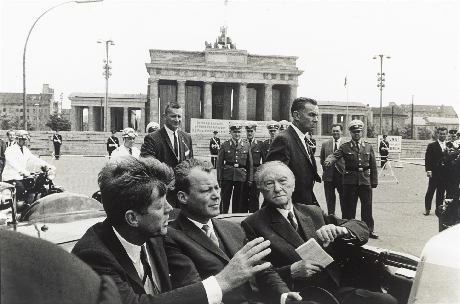 Will McBride. „John F. Kennedy, Willy Brandt, Konrad Adenauer vorm Brandenburger Tor, Berlin“. 1963