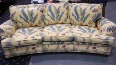 A mid 20th century curved three seat sofa upholstered with floral designs against a yellow ground.