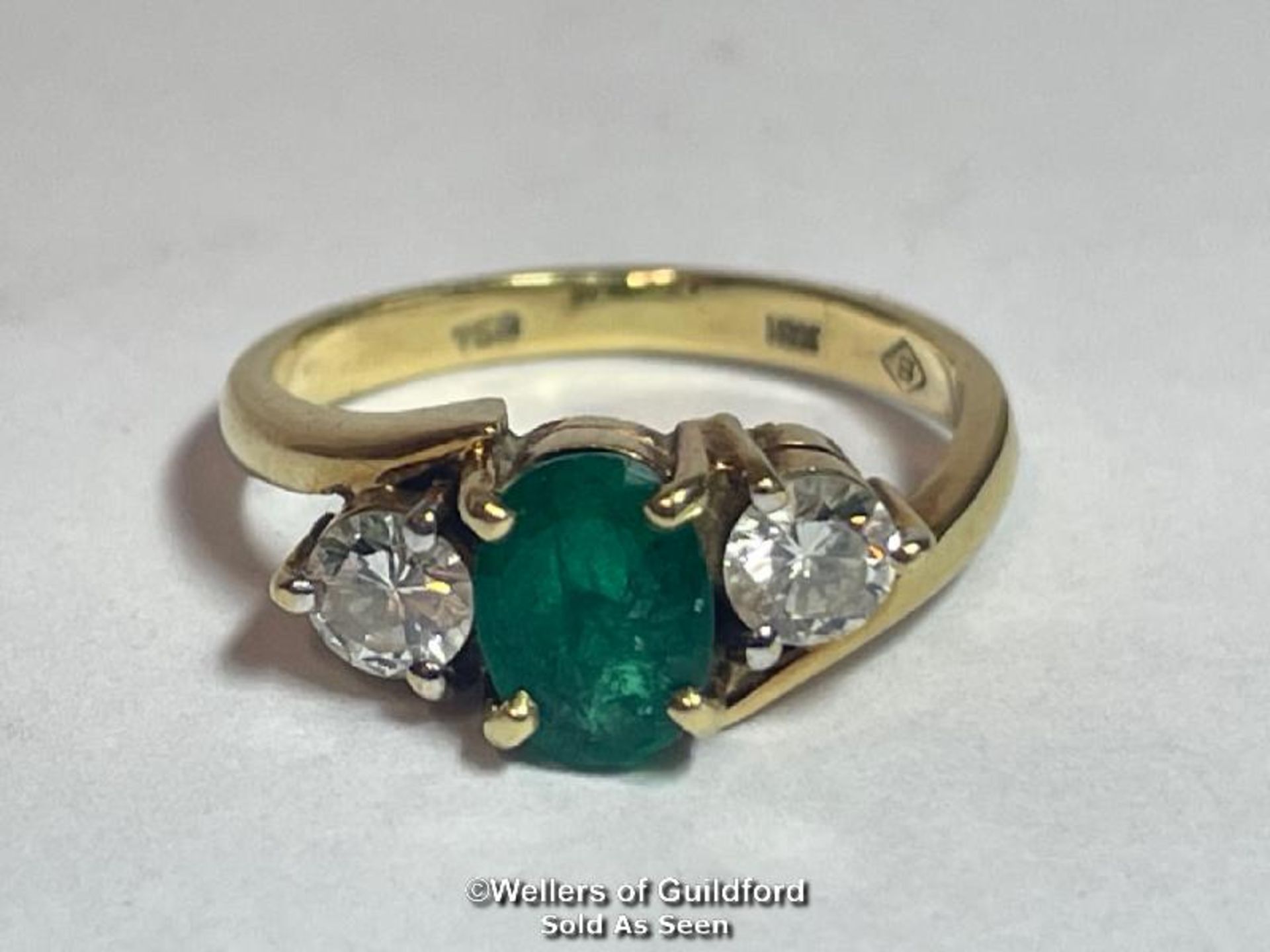 AN EMERALD AND DIAMOND THREE STONE RING IN CROSSOVER STYLE. EMERALD MEASURES APPROX 6.9 X 5.1 X 3.