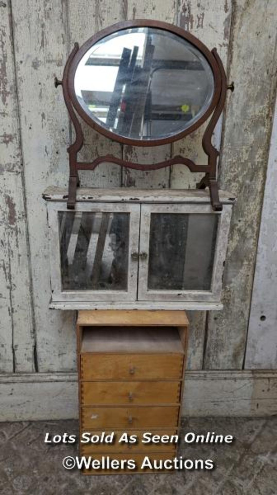 An oval mirror on stand, a set of drawers (top drawer missing) and a glazed wall cupboard with