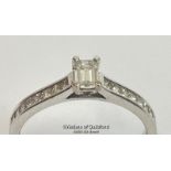 An emerald cut diamond solitaire ring with diamond shoulders, in hallmarked 18ct white gold.