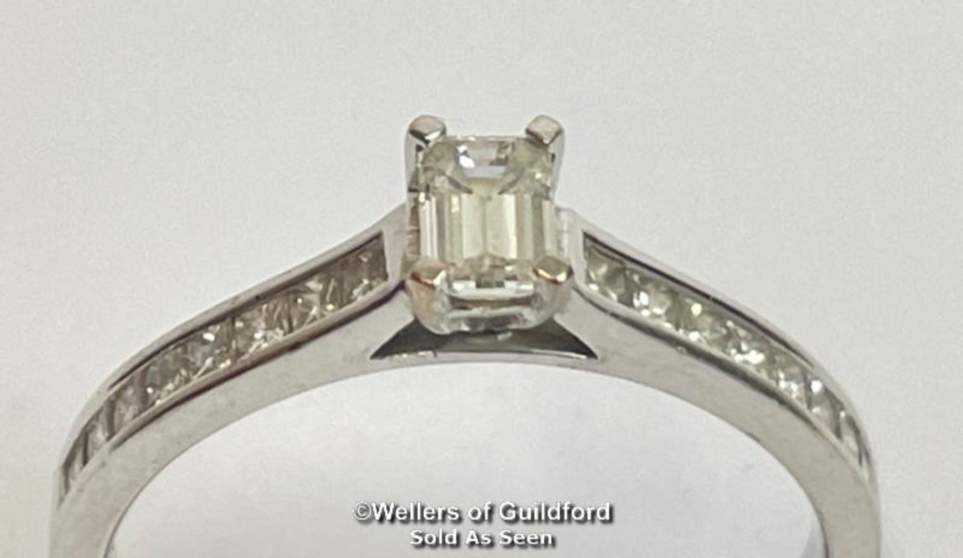 An emerald cut diamond solitaire ring with diamond shoulders, in hallmarked 18ct white gold.