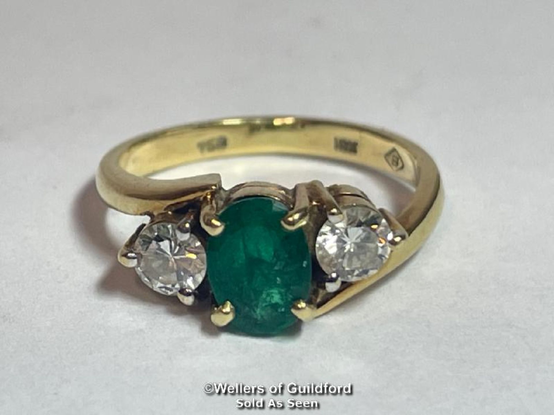 An emerald and diamond three stone ring in crossover style. Emerald measures approx 6.9 x 5.1 x 3.