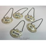 A matching set of five ceramic bottle labels inscribed port, sherry, brandy, gin and scotch on metal