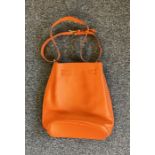 An orange leather shoulder bag in the style of the Kelly design, marked "Hermes".