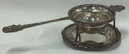 A decorative Continental silver chased tea strainer on stand.