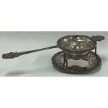 A decorative Continental silver chased tea strainer on stand.