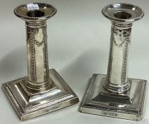 A pair of silver square based candlesticks with sw