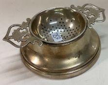 A silver tea strainer on stand.