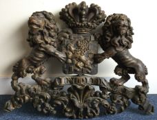 A large carved wooden coat of arms with crown finial and scroll decoration and crested centre.