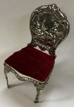 A large silver pin cushion in the form of a chair with embossed decoration.