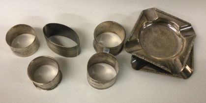 A collection of silver napkin rings together with a pair of ashtrays.