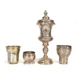 A Continental metalware covered goblet with wreath decoration, h. 25 cm, two beakers and a dish,