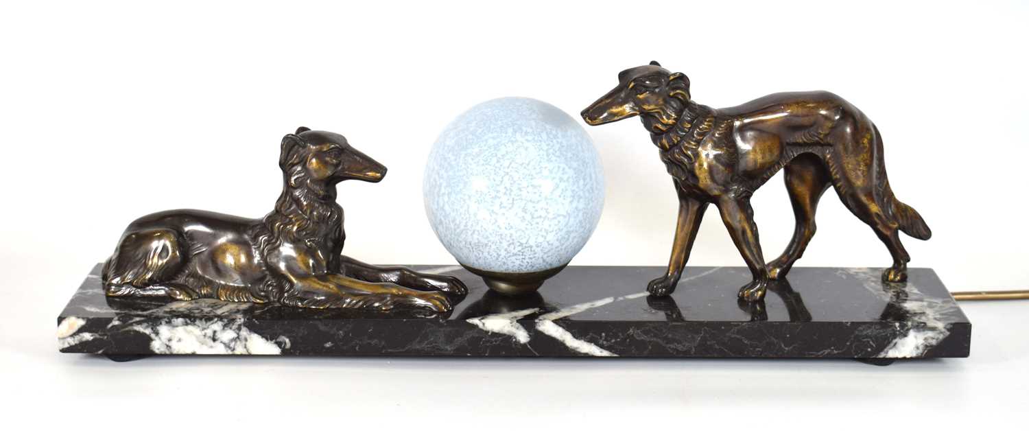 An Art Deco style lamp, the spherical glazed shade flanked by a pair of spelter dogs, on a marble