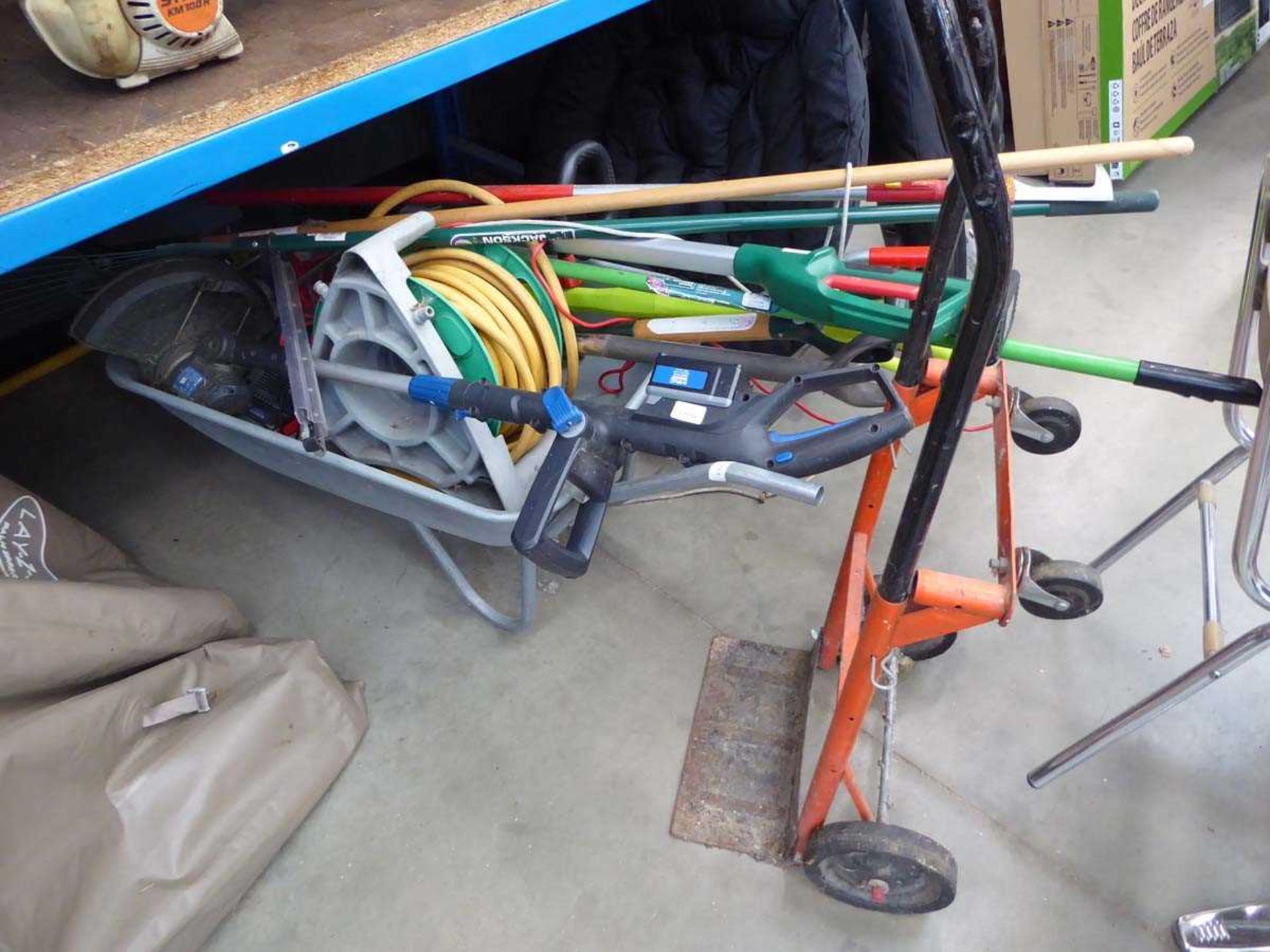 Galvanised wheelbarrow containing various garden tools including battery powered hedge cutters,