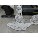 Concrete mermaid sitting on rock with concrete crocodile