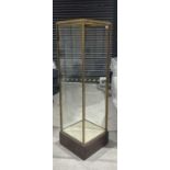 +VAT Column shaped brass framed display cabinet with adjustable shelving, mounted on a dark oak