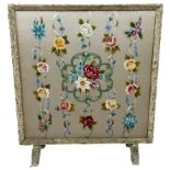 A CREWEL WORK EMBROIDERED TEXTILE FIRESCREEN, mounted in a faux shell frame on two short legs.